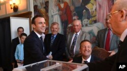 Presiden Perancis Emmanuel Macron, kiri, bersalaman dengan petugas pemilu setelah memberikan suaranya pada putaran kedua pemilu parlemen Perancis di Le Touquet, Perancis utara, Minggu, 18 Juni 2017. (Christophe Archambault/Pool Photo via AP)