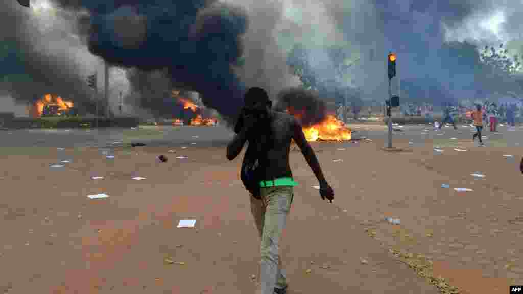 Un manifestant essuie son visage devant le parlement alors que des voitures et des documents brûlent à l&#39;extérieur, à Ouagadougou le 30 octobre, 2014. Des centaines de manifestants en colère au Burkina Faso ont pris d&#39;assaut le parlement le 30 Octobre avant d&#39;y mettre le feu en signe de protestation contre l&#39;intention de modifier la Constitution pour permettre au Président Blaise Compaoré pour étendre son règne de 27 ans. AFP PHOTO / ISSOUF SANOGO 