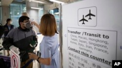 មន្ត្រីសុខាភិបាលថៃម្នាក់កំពុងពិនិត្យសីតុណ្ហភាពភ្ញៀវទេសចរ ខណៈដែលពួកគេមកដល់អកាសយានដ្ឋាន Suvarnabhumi ទីក្រុងបាងកក ថៃ កាលពីថ្ងៃ៤ ខែមីនា ឆ្នាំ២០២០។ 