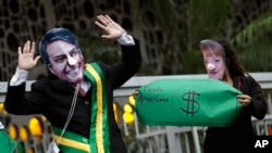 FILE - Demonstrators wear masks of Brazil's President Jair Bolsonaro, left, and Germany's Chancellor Angela Merkel during a protest in defense of the Amazon in Rio de Janeiro, Brazil, Sept. 5, 2019.