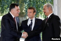French President Emmanuel Macron stands between Libyan Prime Minister Fayez al-Sarraj (L), and General Khalifa Haftar (R), commander in the Libyan National Army (LNA), who shake hands after talks over a political deal to help end Libya’s crisis in La Celle-Saint-Cloud near Paris, July 25, 2017.