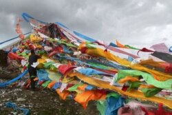 FILE - A Tibetan man ties prayer flags to a shrine at the foot of the Amnye Machen mountains on the eastern edge of the Tibetan Plateau in northwestern China's Qinghai Province, Aug. 20, 2018.