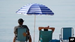 People relax under a sun shade on the beach during a hot morning at Bournemouth, southern England, July 20, 2021. (Andrew Matthews/PA via AP)