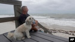 Kent Ejren i njegov pas Blanko posmatraju talase koje donosi tropska oluja Isaias, u blizini Džejsi bič parka, 2. avgusta 2020, u Vero Biču, Florida.