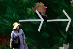 A woman with a face mask to help curb the spread of the coronavirus walks past a wall with arrows in Tokyo, May 5, 2020.