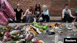 Women sit by an impromptu memorial of flowers commemorating the victims at the scene of the car attack on a group of counterprotesters during the "Unite the Right" rally as people continue to react to the weekend violence in Charlottesville, Virginia, Aug. 14, 2017.