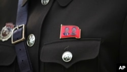 A North Korean guide wears a pin with the photos of late North Korean leaders Kim Il Sung at left and Kim Jong Il at right, Aug. 17, 2018, at the Samjiyon Great Monument in Samjiyon, North Korea.