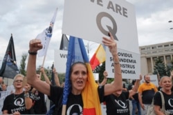 Romanian supporters of QAnon shout slogans against the government's measures to prevent the spread of the COVID-19 infections, like wearing a face mask, during a rally in Bucharest, Romania, Monday, Aug. 10, 2020.