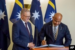 Australian Prime Minister Anthony Albanese looks on as Nauru President David Adeang, right, signs the Australian Parliament House guest book in Canberra, Dec. 9, 2024.