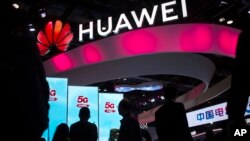 Para peserta berjalan melewati layar untuk layanan 5G dari perusahaan teknologi China Huawei di PT Expo di Beijing. (Foto: AP)