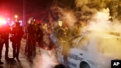 Polisi mendekati mobil polisi setelah seorang demonstran melemparkan alat berasap di Ferguson, Missouri (25/11). (AP/David Goldman)