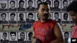 Asian workers walk past images of political prisoners plastered on a wall in Malkiya village, Bahrain, Nov. 4, 2015. Bahrain says it has arrested 47 suspects and seized explosives in a counter terrorism operation, and has again alleged Iranian involvement in militant attacks. 