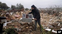 Seorang pria Palestina memungut foto keluarga yang rumahnya dihancurkan Israel di antara puing-puing rumah mereka di Sheikh Jarrah, Yerusalem (19/1).