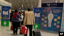 FILE - Travelers pass by a health checkpoint before entering immigration at the international airport in Beijing, Jan. 13, 2020.