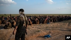 Kombatan Pasukan Demokratik Suriah yang didukung AS, berjaga di dekat para pria yang menunggu untuk diperiksa setelah dievakuasi dari wilayah terakhir ISIS, dekat Baghuz, timur Suriah, 22 Februari 2019. 