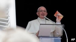 FILE - Pope Francis shows a crucifix during the Angelus noon prayer he delivers from the window of his studio overlooking St. Peter's Square at the Vatican, Sept. 16, 2018.
