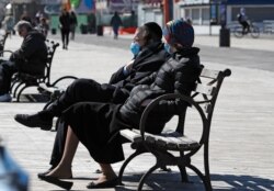 A couple wear face masks as they sit on a bench in the sun April 2, 2020, at the Coney Island boardwalk in the Brooklyn borough of New York.