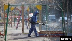 មន្ត្រីសុខាភិបាលម្នាក់ស្ថិតក្នុងសម្លៀកបំពាក់តាមក្បួនវេជ្ជសាស្ត្រ ដើរបាញ់ថ្នាំសម្លាប់មេរោគនៅកន្លែងក្មេងលេងកម្សាន្ត ដើម្បីទប់ទល់នឹងការឆ្លងរាលដាលនៃវីរុសកូវីដ១៩ នៅទីក្រុង Almaty ប្រទេសកាហ្សាក់ស្ថាន ថ្ងៃទី២៧ ខែមីនា ឆ្នាំ២០២០។ 