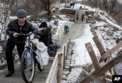 Local residents walk across a bridge damaged during fighting between Ukrainian government forces and Russia-backed rebels in Stanytsia Luhanska, Luhansk region, eastern Ukraine, Jan. 16, 2016.