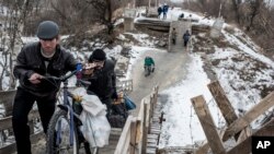 FILE - Local residents walk across a bridge damaged during fighting between Ukrainian government forces and Russia-backed rebels in Stanytsia Luhanska, Luhansk region, eastern Ukraine, Jan. 16, 2016.