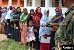 FILE - Seorang anak perempuan mengamati petugas saat mengikuti ibunya menyalurkan hak pilihnya di salah satu TPS di distrik Sepahijala, Tripura, India, 12 Mei 2019.