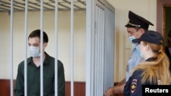 Former U.S. Marine Trevor Reed, who was detained in 2019 and accused of assaulting two police officers, stands inside a defendant's cage during a court hearing in Moscow, Russia, July 30, 2020. 