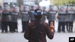 បាតុករ​ស្រី​ម្នាក់​លើក​ម្រាម​ដៃ​បី​ឡើង​នៅ​មុខ​ប៉ូលិស​ក្នុង​ទីក្រុង Mandalay ប្រទេស​មីយ៉ាន់ម៉ា ថ្ងៃទី២០ ខែកុម្ភៈ ឆ្នាំ២០២១។