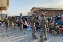U.S. soldiers stand guard as Afghan people wait to board a U.S. military aircraft to leave Afghanistan, at the military airport in Kabul, August 19, 2021.