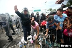 FILE - A police officer helps a Honduran migrant, part of a caravan trying to reach the U.S., as she storms a border checkpoint to cross into Mexico, in Ciudad Hidalgo, Mexico, Oct. 19, 2018.