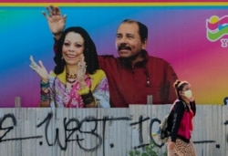 Seorang perepuan mengenakan masker berjalan di depan murał Presiden Nikaragua Daniel Ortega dan Wakil Presiden Rosario Murillo di Managua, Nikaragua, 27 Maret 2020. (REUTERS/Oswaldo)