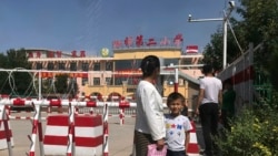 In this Aug. 31, 2018, file photo, a child and a woman wait outside a school entrance mounted with surveillance cameras and barricades with multiple layers of barbed wire in Peyzawat, western China's Xinjiang region. (AP Photo/Ng Han Guan, File)