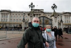 A couple wear face masks as they visit Buckingham Palace in London, Saturday, March 14, 2020.
