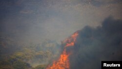Flames rise next to a house as a wildfire burns in the village of Sinterina, Greece, Aug. 16, 2021.