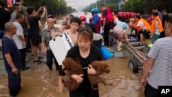 A woman carries her pet dogs as residents are evacuated on rubber boats through floodwaters in Zhuozhou in northern China's Hebei province, southwest of Beijing, on Aug. 2, 2023.