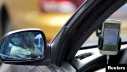 Seorang pengemudi taksi (nampak di kaca spion mobil) menggunakan 'Didi Chuxing', aplikasi telepon untuk pemanggilan layanan taksi di Beijing, China (22/6).