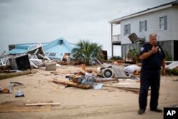 FILE - The remnants of a home leveled by Hurricane Matthew sit along the beachfront as Chief of Police George Brothers talks on the radio after Hurricane Matthew hit Edisto Beach, S.C., Oct. 8, 2016.