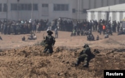 Israeli soldiers, on the Israeli side of the border with the Gaza Strip, watch Palestinian protesters, in Gaza, May 14, 2018.