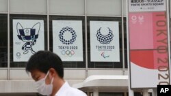 Seorang pria mengenakan masker berjalan melewati poster Olimpiade Tokyo di Tokyo, Jepang, 7 JUni 2021. (AP Photo/Koji Sasahara)
