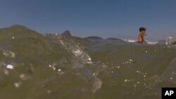 Seorang anak laki-laki mengarungi air laut di pantai Flamengo, Rio de Janeiro (28/7). (AP/Leo Correa)
