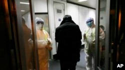 Health Officials in hazmat suits wait at the gate to check body temperatures of passengers arriving from the city of Wuhan, Jan. 22, 2020, at the airport in Beijing, China. 
