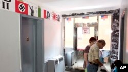 FILE - Residents of an apartment building pass posters of Adolf Hitler and Benito Mussolini in the hallway as they enter an apartment, Aug. 23, 2017, in the Queens borough of New York. New York City Councilman Jimmy Van Bramer protested the display of anti-semitic posters in the building. 