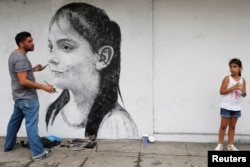 Ariadna Herrera, 6, poses for Cuban artist Maisel Lopez as he paints the wall of a state art gallery in Havana, April 18, 2017.