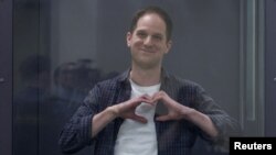 Reporter Wall Street Journal Evan Gershkovich, yang ditahan atas tuduhan spionase, membuat gerakan berbentuk hati di balik dinding kaca saat sidang pengadilan di Moskow, Rusia, 23 April 2024. (Foto: Reuters )