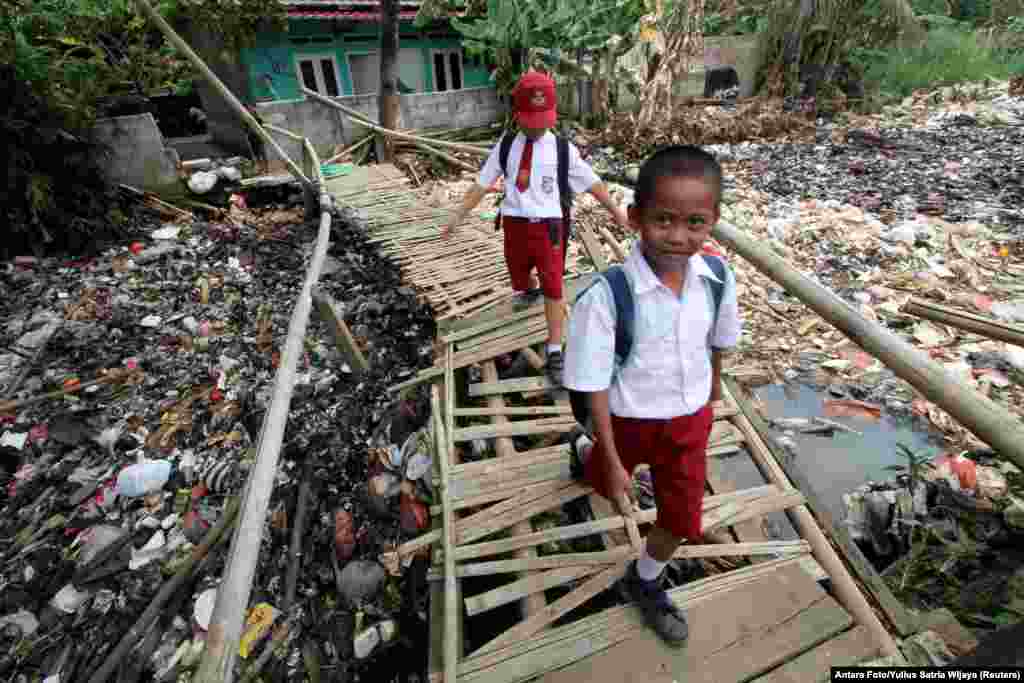 Students cross a bamboo bridge, above a garbage-filled stream branching off the Ciliwung River, in Bogor, Indonesia.