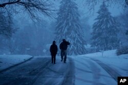 Residents walk down a snowy street during a winter storm, March 2, 2018, in Marple Township, Pa.