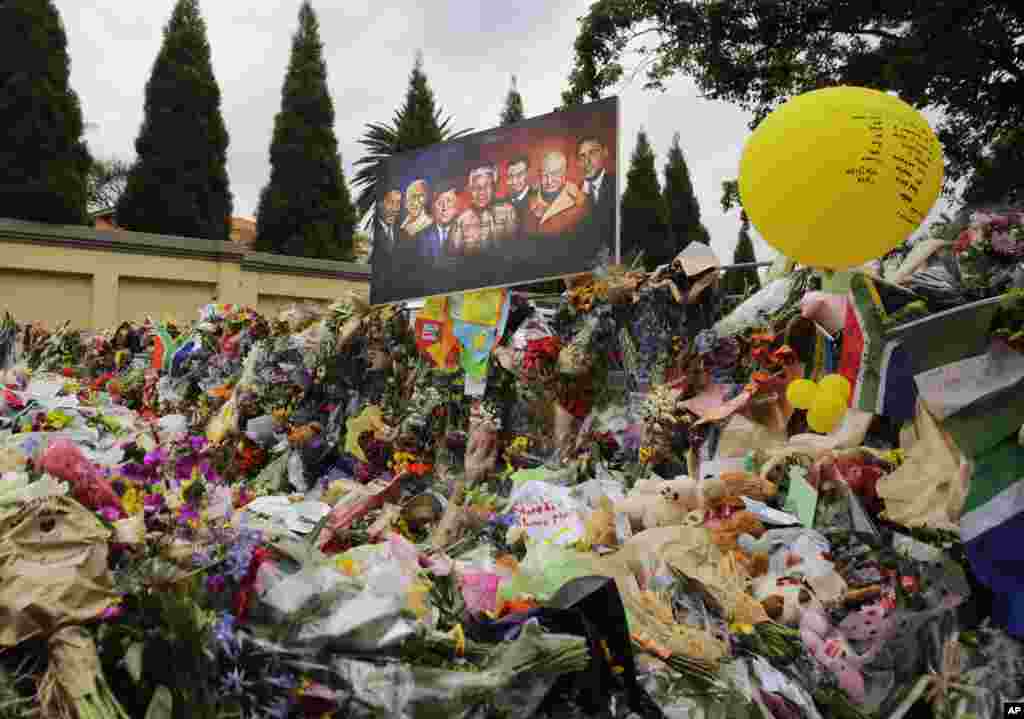 A painting of Nelson Mandela surrounded by Martin Luther King, Mohandas Gandhi, John F. Kennedy, Abraham Lincoln, Winston Churchill and Barack Obama is fixed on top of flowers outside his home in Johannesburg, Dec. 9, 2013. 