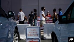 FILE - A sign indicates where mail ballots may dropped off as people wait in line at one of the few in-person voting places during a nearly all-mail primary election in Las Vegas, June 9, 2020.