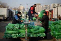 Para pedagang mengenakan masker saat memindahkan sayuran di pasar grosir, di tengah pandemi COVID-19 di Beijing, China, 19 Februari 2020.
