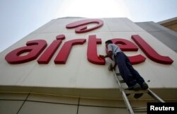 FILE - A worker cleans a logo of Bharti Airtel at its zonal office building in the northern Indian city of Chandigarh.