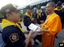 A Thai policeman checks identity card of a Buddhist monk of the Dhammakaya sect temple for security outside the temple in Pathum Thani, north of Bangkok, Thailand, Feb. 22, 2017.